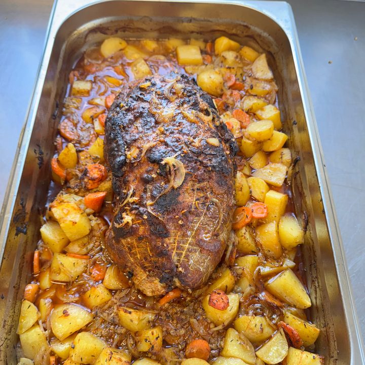 Rôti de porc doré au four sur pommes de terre, carottes et oignons à la boulangère